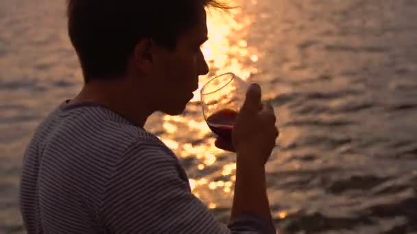 Uomo che beve bottiglia di vino durante il tramonto vicino al mare, rallentatore — Video Stock