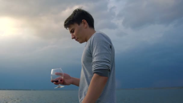 Joven bebiendo vino al atardecer junto al mar — Vídeo de stock