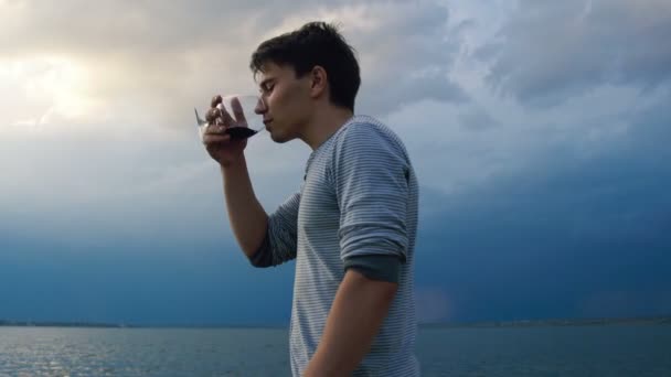 Jeune homme buvant du vin au coucher du soleil au bord de la mer — Video