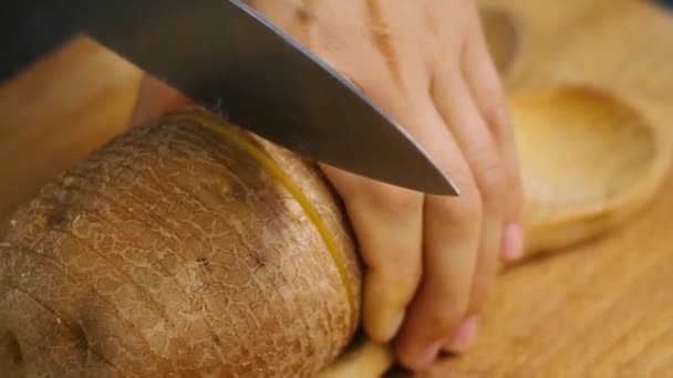 Close-up de uma mão de mulheres descascando grandes batatas em uma placa de corte de madeira com uma faca de cozinha. Conceito de preparar batatas e prepará-las para cozinhar — Vídeo de Stock
