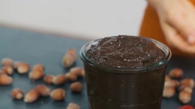Sağlıklı kakao ve fındık kreması yakın çekim. Bir kadının eli, bardağa fındık ve tatlı atar. Kakao tozu, çikolata ve fındık..