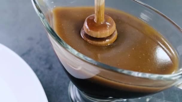 Süßer Sirup wird mit einem Honiglöffel oder einem Stock gegossen. Honigstange im Glas mit brauner Flüssigkeit. — Stockvideo