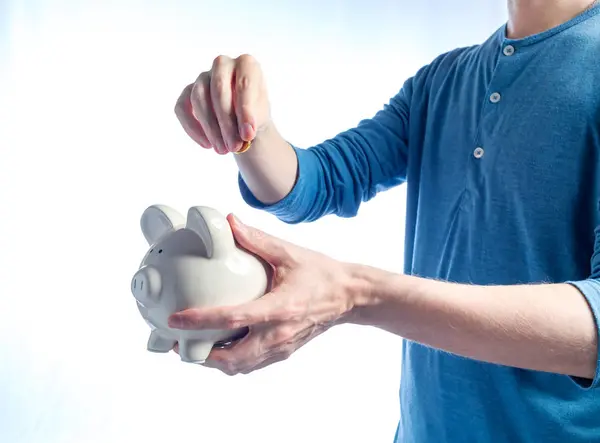 Hombre con una alcancía y una moneda en sus manos —  Fotos de Stock