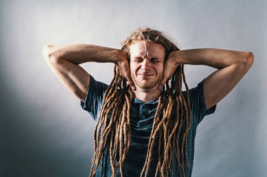 Genç adam sağlam bir arka plan üzerinde kulakları engelleme