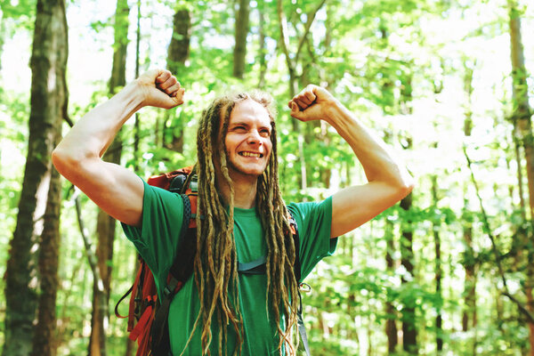 Happy hiker raising his hands in the air in a victory salute in the forest
