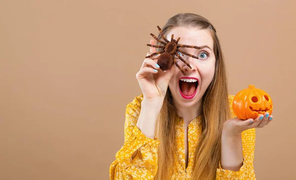 Young woman holding a halloween pumpkin and a spider