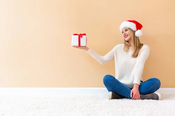 Noel Baba şapkalı genç bir kadın elinde bir hediye kutusu tutuyor. — Stok fotoğraf