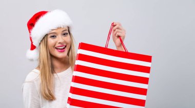 Elinde alışveriş çantası tutan Noel Baba şapkalı genç bir kadın.