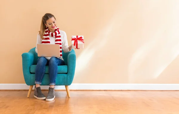 Young woman with a laptop computer holding a Christmas gift box — Stock Photo, Image