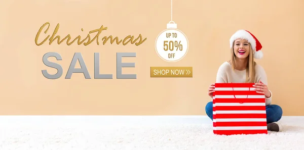 Christmas sale message with woman with Santa hat holding a shopping bag — Stock Photo, Image