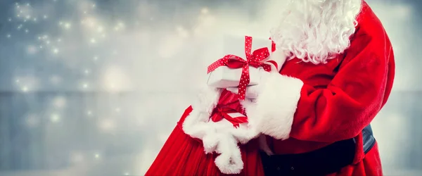 Der Weihnachtsmann hält eine Geschenkschachtel aus einem roten Sack — Stockfoto
