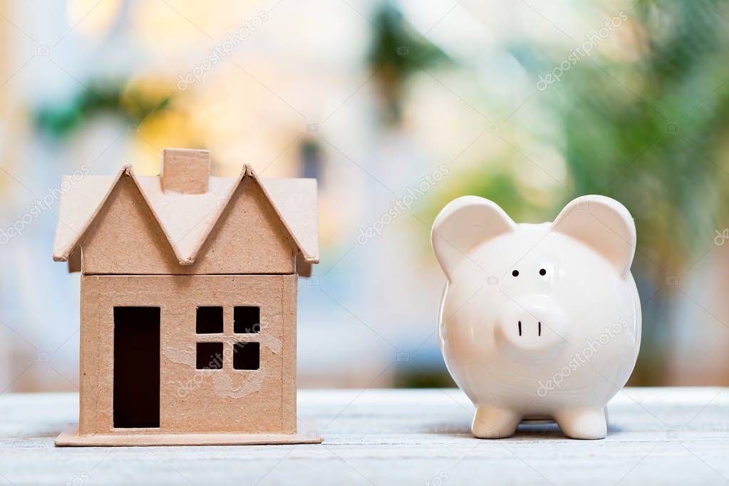 Piggy bank and model house on a bright background