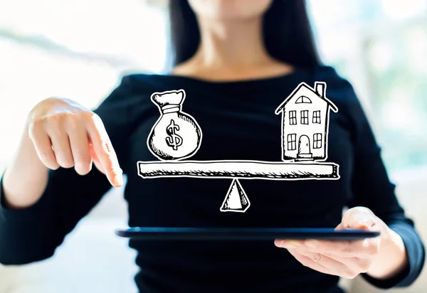 Casa e dinheiro na escala com mulher usando tablet — Fotografia de Stock
