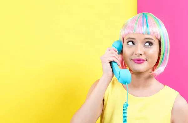 Jonge vrouw in een kleurrijke pruik praten over een retro telefoon — Stockfoto