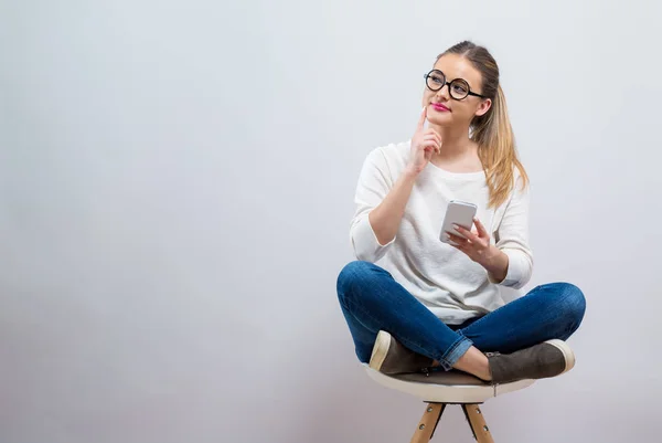 Junge Frau mit ihrem Handy denken — Stockfoto