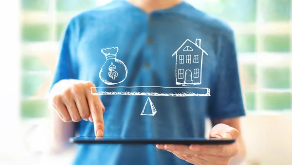 Casa y dinero en la balanza con el hombre usando una tableta — Foto de Stock