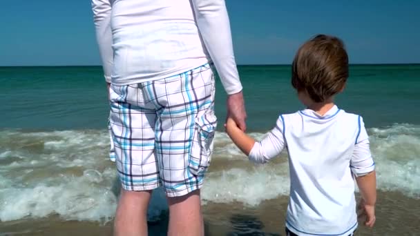 Niño agarrado de la mano con su padre en la orilla del mar — Vídeo de stock