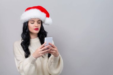 Noel Baba şapkalı genç bir kadın akıllı telefonunu kullanıyor.