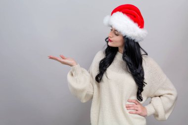 Noel Baba şapkalı genç kadın bir şey gösteriyor.