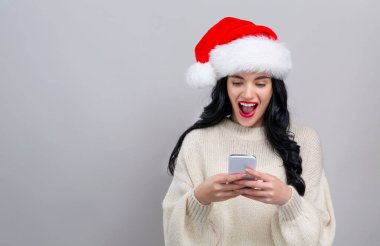 Noel Baba şapkalı genç bir kadın akıllı telefonunu kullanıyor.