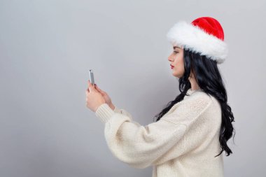 Noel Baba şapkalı genç bir kadın akıllı telefonunu kullanıyor.