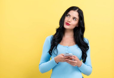 Akıllı telefonu olan mutlu genç bir kadın bir şeyler düşünüyor.