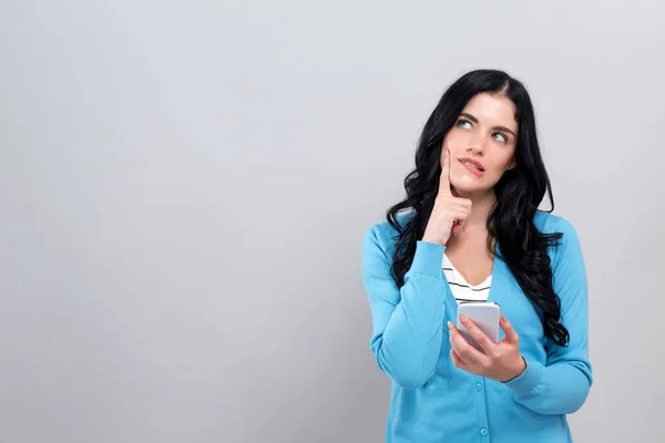 Jonge vrouw met smartphone denken over iets — Stockfoto