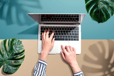 Tropikal yaprakları olan bir dizüstü bilgisayar kullanan kişi