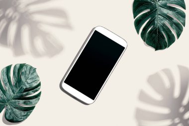 Tropikal canavar yaprakları ve gölgesi olan akıllı telefon.