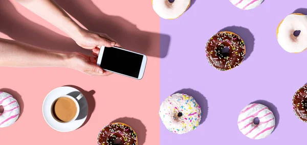 Persoon met een smartphone met donuts — Stockfoto