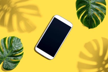 Tropikal canavar yaprakları ve gölgesi olan akıllı telefon.