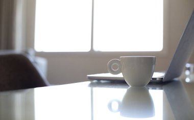 Laptop bilgisayarın yanında beyaz kahve kupası.