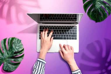 Tropikal yaprakları olan bir dizüstü bilgisayar kullanan kişi