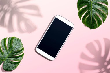 Tropikal canavar yaprakları ve gölgesi olan akıllı telefon.