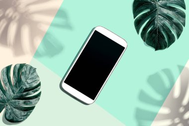 Tropikal canavar yaprakları ve gölgesi olan akıllı telefon.
