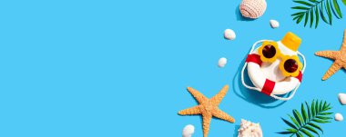 Güneş gözlüğü takan güneş kremi şişesi, deniz yıldızı ve deniz kabuğu.