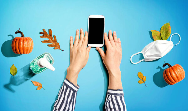 Smartphone with mask and sanitizer bottle in Autumn
