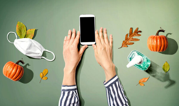 Smartphone with mask and sanitizer bottle in Autumn