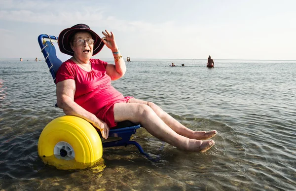 View on the happy old lady in a wheelchair on the beach on a sunny day