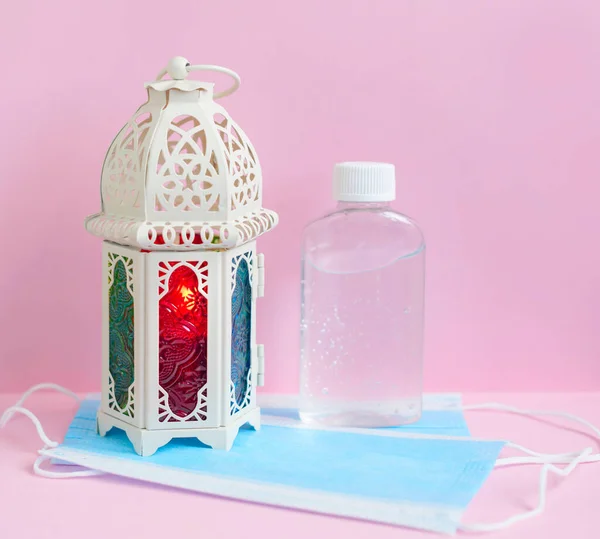 lantern with candle and face mask with sanitizer on pink background for Ramadan holy month for Muslims in 2020 in quarantine and self isolation due to the coronavirus pandemic