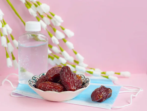 dates, protective mask and sanitizer on pink background for Ramadan holy month for Muslims in 2020 in quarantine and self-isolation due to the coronavirus pandemic