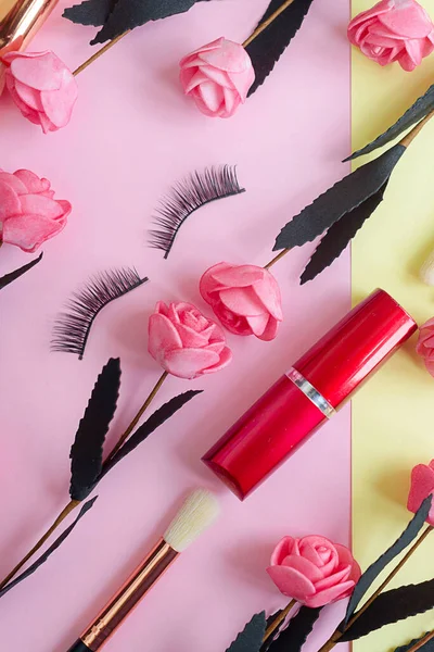 premium makeup brushes, lipstick and  false eyelashes on a colored pink and yellow background, creative cosmetics flat lay