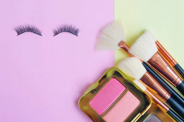 premium makeup brushes and  false eyelashes on a colored pink and yellow background, creative cosmetics flat lay
