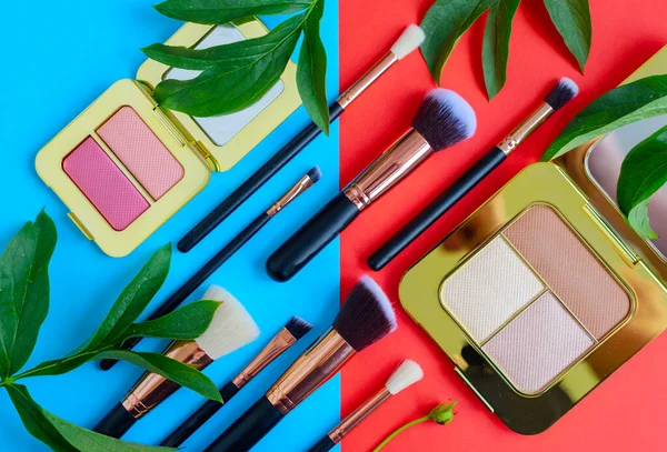 premium makeup brushes, eye shadow palette and leaves on a colored blue and red background, creative cosmetics flat lay with diagonal composition