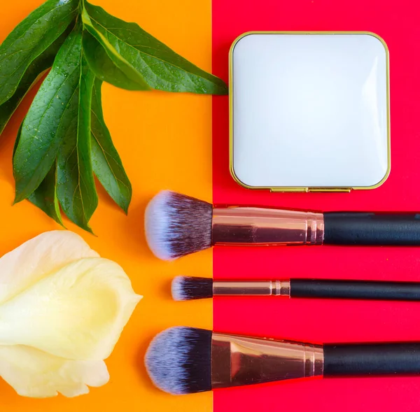 premium makeup brushes and blush on a colored red and orange background, creative cosmetics flat lay, copy space