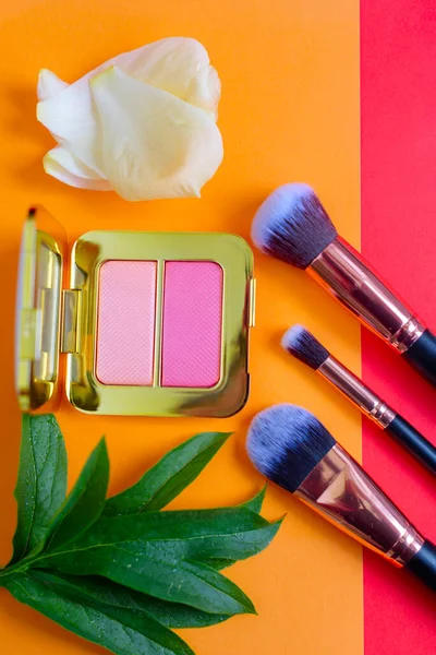 premium makeup brushes and blush on a colored red and orange background, creative cosmetics flat lay, copy space