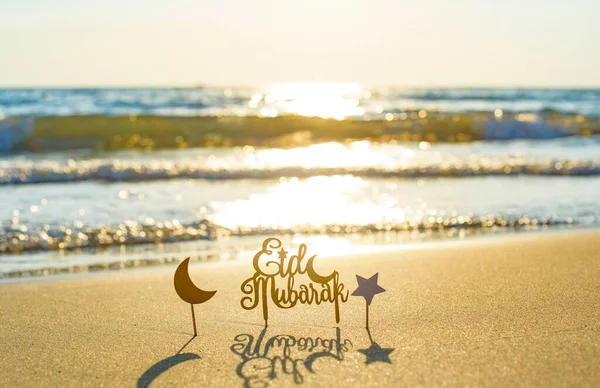 text Eid Mubarak (in English Happy Holidays) on the sand by the sea