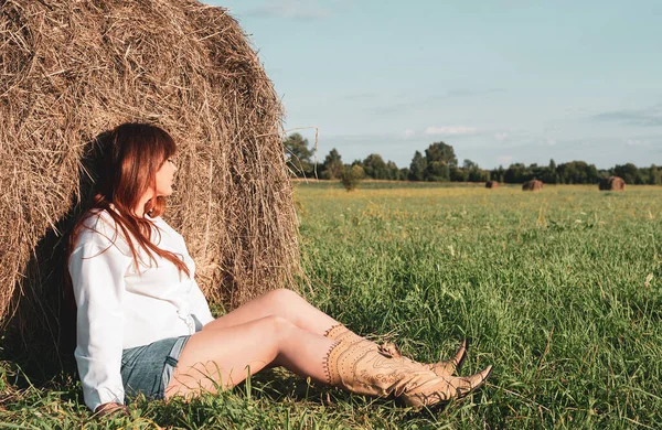 female model plus size on a field with haystacks, a beautiful young woman with brown hair in short shorts and a white shirt, harvest concept