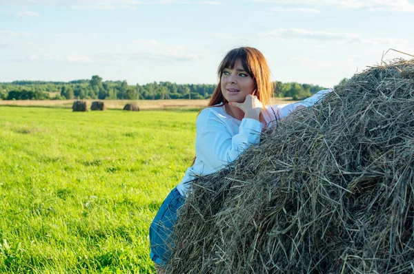 female model plus size on a field with haystacks, a beautiful young woman with brown hair in short shorts and a white shirt, harvest concept