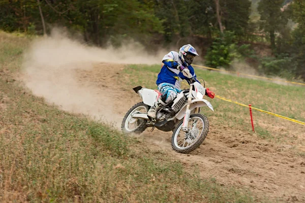 a driver runs fast in downhill leaving a trail of dust riding his motocross bike during the motorcycle rally 